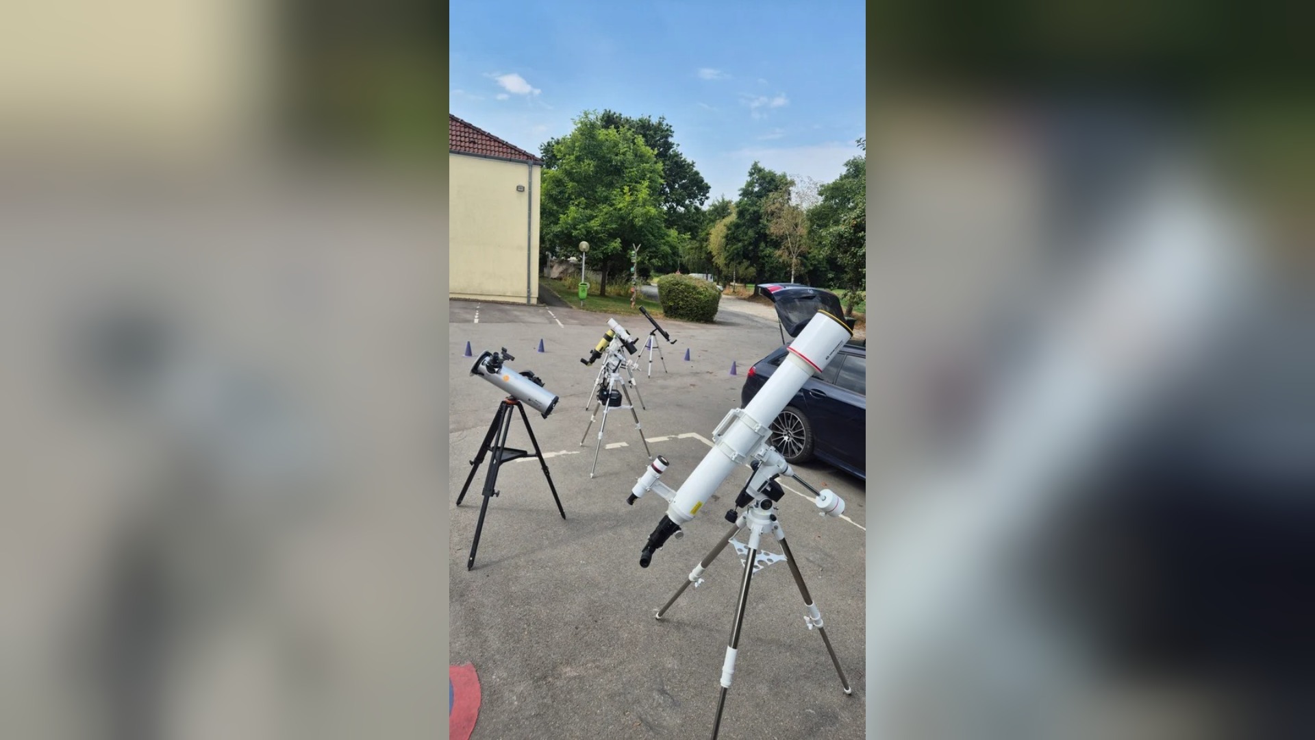 Mehrere Teleskope auf einem asphaltierten Platz vor einem Gebäude und Bäumen, für Sonnenbeobachtung aufgestellt