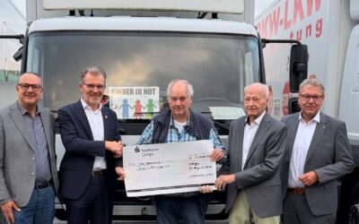 Fünf Männer halten einen Spendenscheck der Sparkasse Lemgo über 3.000 Euro vor Lastwagen der Organisation Kinder in Not