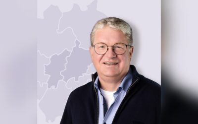 Frank Sommerfeld, ein lächelnder Mann mit grauen Haaren und Brille, in blauem Hemd und Pullover vor einer Karte