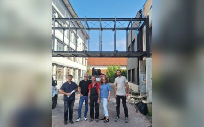 Fünf Personen stehen unter der neuen Stahl-Verbindungsbrücke zwischen zwei Gebäuden der Grundschule Helpup