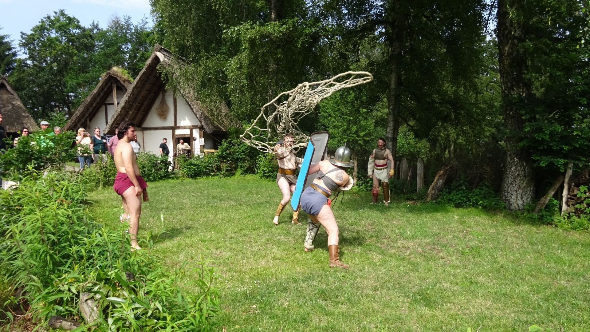 Zwei Männer in Gladiatorenkostümen kämpfen auf einer Wiese, einer wirft ein Netz, der andere wehrt mit Schild ab