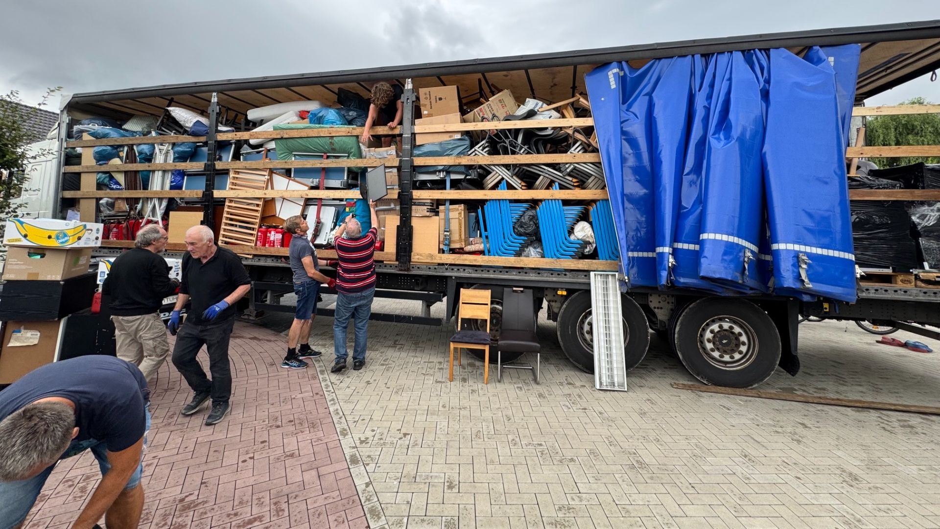 Helfer beladen einen großen LKW mit Spenden wie Möbeln, Kartons und Stühlen für einen Hilfstransport