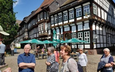 Senioren stehen auf einem sonnigen Kopfsteinpflasterplatz vor dem historischen Gasthaus Brodhaus und weiteren