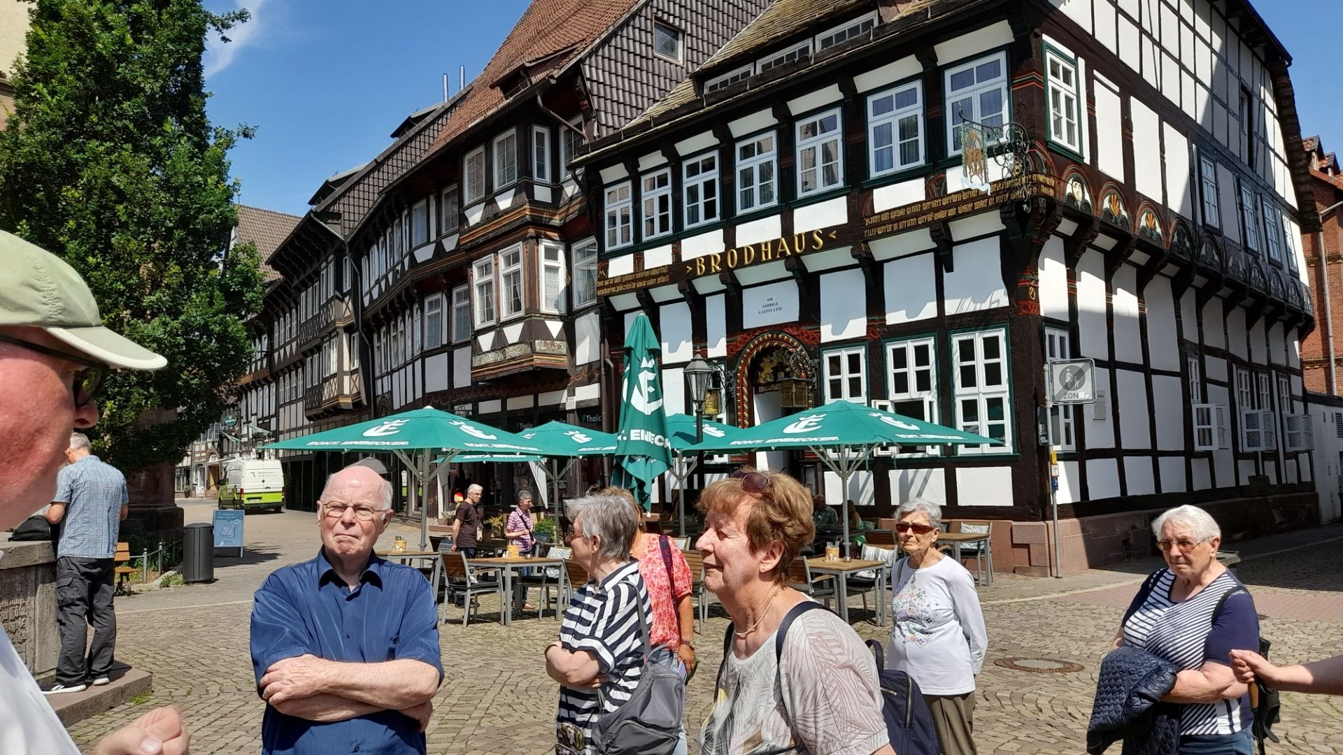 Senioren stehen auf einem sonnigen Kopfsteinpflasterplatz vor dem historischen Gasthaus Brodhaus und weiteren