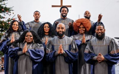 Neun lächelnde Personen der New York Gospel Stars in grauen Roben, manche mit erhobenen oder gefalteten Händen, vor