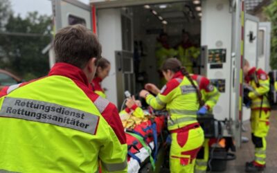 Rettungsteam in gelber Schutzkleidung versorgt eine Person auf einer Trage vor einem Rettungswagen