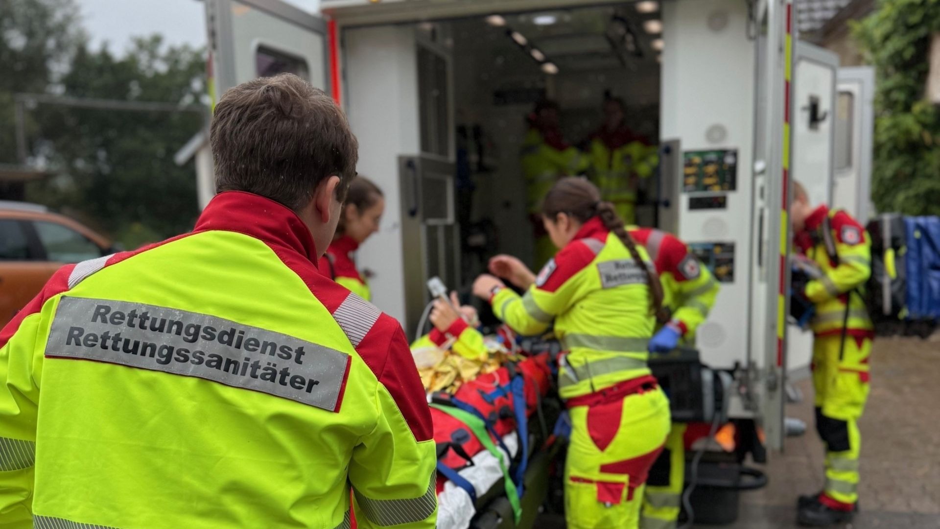 Rettungsteam in gelber Schutzkleidung versorgt eine Person auf einer Trage vor einem Rettungswagen