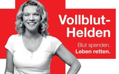 Lächelnde Frau mit Pflaster am Arm vor rotem Hintergrund mit DRK-Kreuz und dem Text Vollblut-Helden, Blut spenden