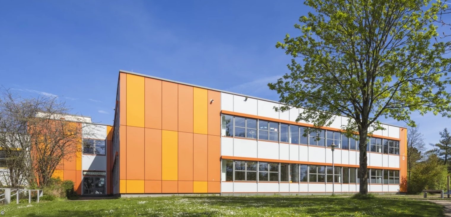 Modernes orange-weißes Schulgebäude mit vielen Fenstern und einem Baum davor auf grünem Gras unter blauem Himmel