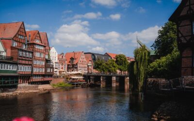 Fachwerkhäuser und Restaurants am Lüneburger Stintmarkt am Flussufer mit einer Brücke und Menschen unter blauem Himmel