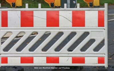Rot-weiß gestreifte Baustellenabsperrung mit gelber Warnleuchte auf dunklem Asphalt