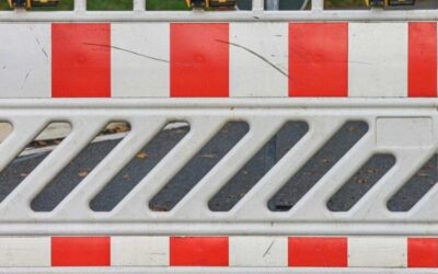 Eine rot-weiße Baustellenabsperrung mit einer orangefarbenen Warnleuchte steht auf einer asphaltierten Straße