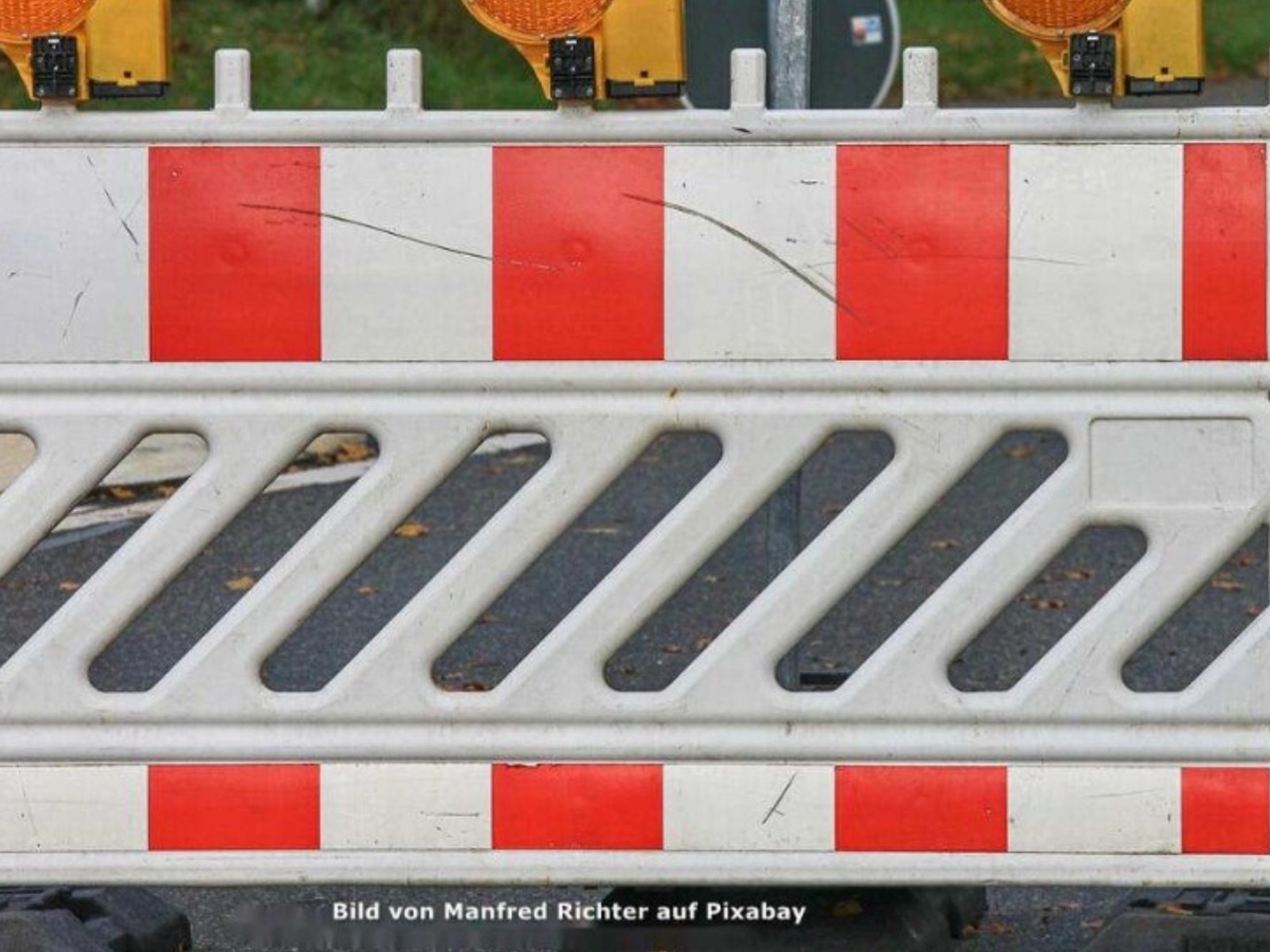 Eine rot-weiße Baustellenabsperrung mit einer orangefarbenen Warnleuchte steht auf einer asphaltierten Straße