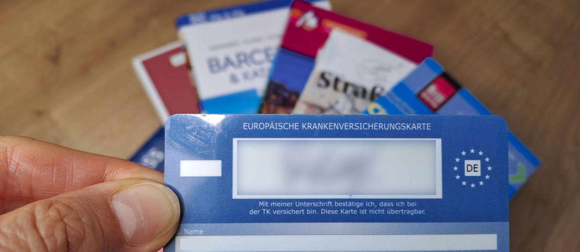 Eine Hand hält eine blaue Europäische Krankenversicherungskarte mit DE-Symbol, im Hintergrund unscharf weitere Karten