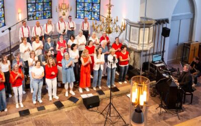 Ein großer Chor aus Männern und Frauen singt und klatscht in einer Kirche, begleitet von Musikern am Keyboard und an