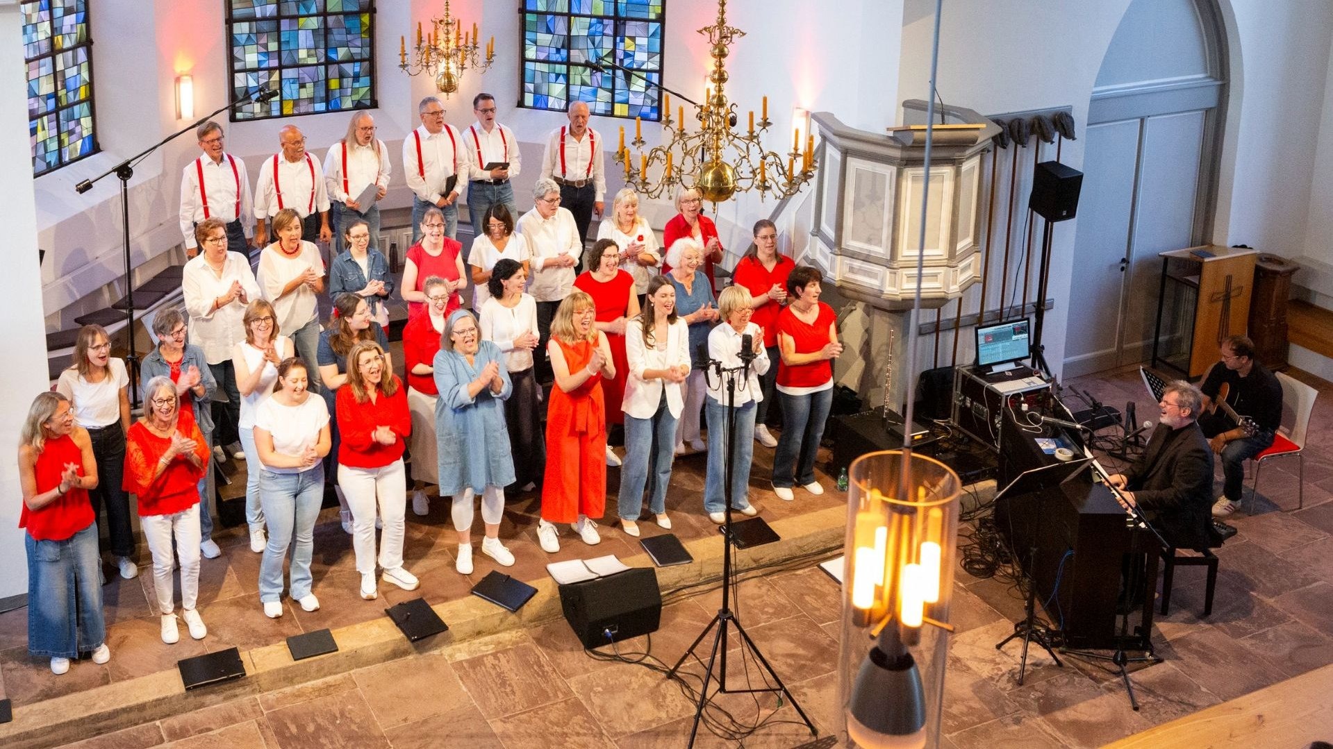 Ein großer Chor aus Männern und Frauen singt und klatscht in einer Kirche, begleitet von Musikern am Keyboard und an