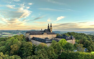 Kloster Banz mit seinen zwei Türmen, umgeben von Wäldern und einer weiten Landschaft unter einem teilweise bewölkten