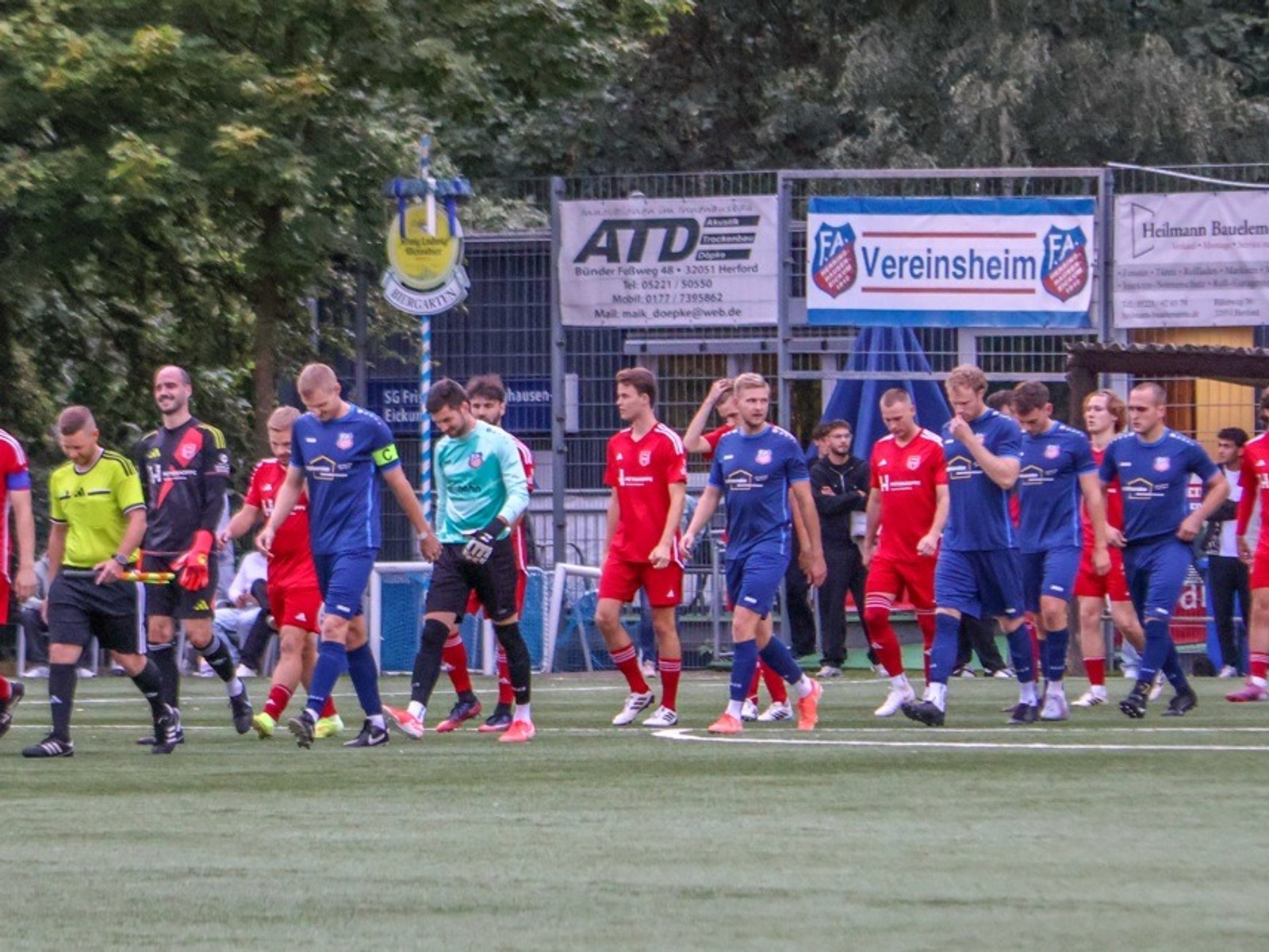 Fußballspieler in roten und blauen Trikots und Schiedsrichter in gelb und schwarz gehen auf grünem Sportplatz