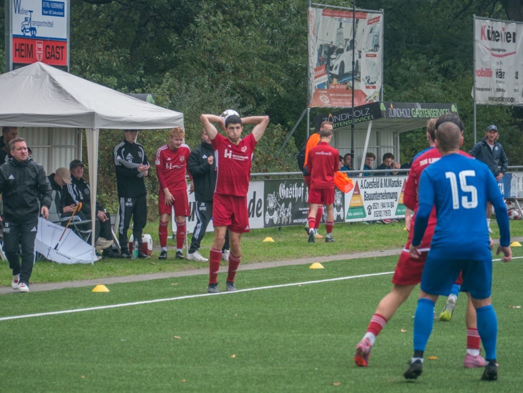 Ein Spieler im roten Trikot macht einen Einwurf, andere Spieler in Rot und Blau sind auf dem Feld