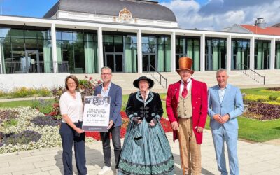 Fünf Personen, zwei davon in historischen Kostümen, stehen im Kurpark Bad Salzuflen vor einem Gebäude und halten ein
