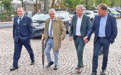 Vier Männer, darunter ein Polizist und Innenminister Herbert Reul, gehen gemeinsam über einen gepflasterten Platz