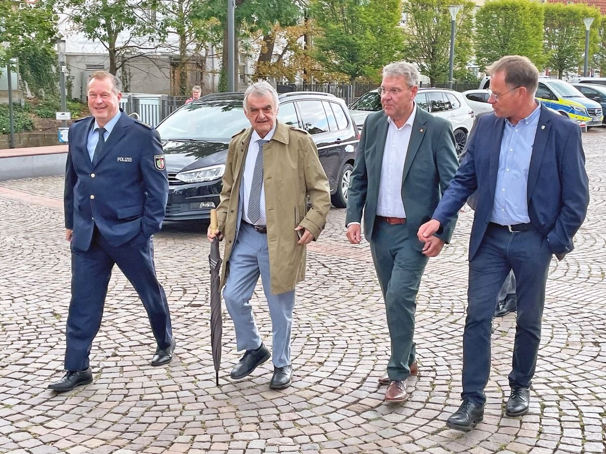 Vier Männer, darunter ein Polizist und Innenminister Herbert Reul, gehen gemeinsam über einen gepflasterten Platz