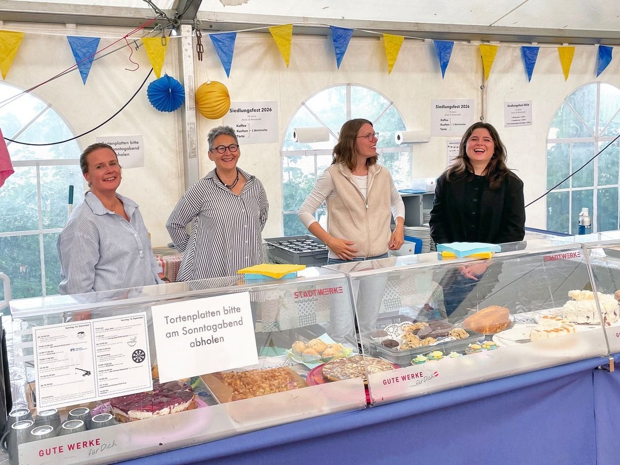 Vier lächelnde Frauen stehen an einem Kuchenstand auf einem Siedlungsfest unter einem Festzelt