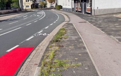 Kurvige Straße mit weißen Radfahrstreifen, einem roten Radwegabschnitt und Bürgersteig vor einem Dönerladen