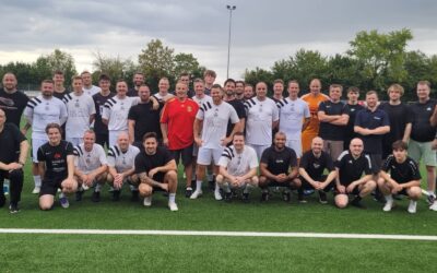 Große Gruppe Männer in Sportkleidung steht lächelnd auf grünem Kunstrasenplatz an einer weißen Linie