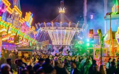 Menschenmenge auf einem nächtlichen Volksfest mit vielen bunten, beleuchteten Fahrgeschäften und einem Kettenkarussell