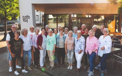 20 lächelnde Erwachsene posieren als Gruppe vor dem Café 104 mit seinen Außentischen
