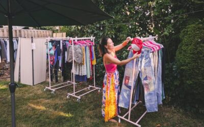 Christin Cornelsen sortiert eine rote Mütze an einem Ständer voller Second-Hand-Kleidung in einem Garten
