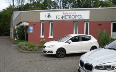 Das Gebäude des Bielefelder TC Metropol mit Schild, roten Wänden und zwei geparkten Autos auf einem gepflasterten