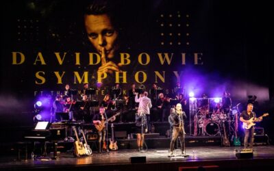 Live-Konzert auf Bühne mit Orchester, Dirigent, Band und Sängern, darüber eine "DAVID BOWIE SYMPHONY"-Leinwand