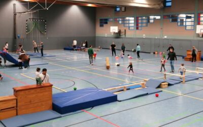 Viele Erwachsene und Kinder spielen und bewegen sich in einer Sporthalle mit aufgebautem Parcours aus Turngeräten und