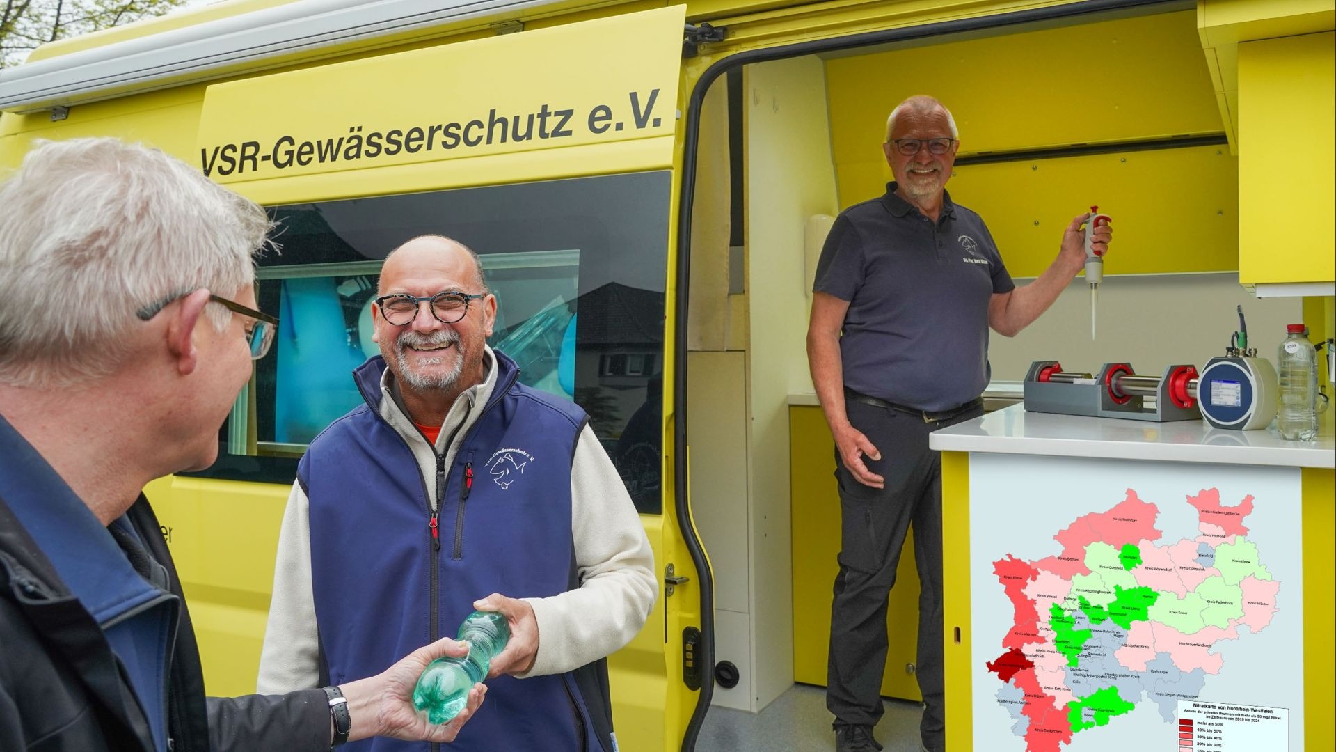 Zwei Männer übergeben und empfangen eine Wasserflasche am gelben VSR-Gewässerschutz Labormobil, ein Dritter steht mit