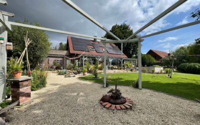 Ein gepflegter Garten mit Kiesweg, Feuerstelle, Rasen, Blumen und einem Haus mit Solardach und Wintergarten