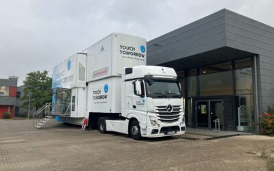 Weißer TouchTomorrow-Truck mit ausgefahrenem Aufbau und Treppe parkt vor einem Gebäude mit „Mensa“-Beschriftung