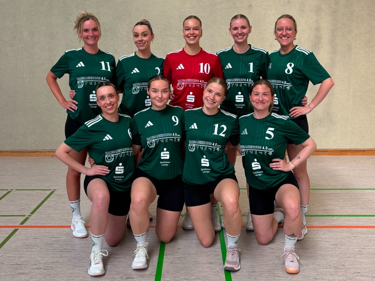 Acht lächelnde Handballspielerinnen in grünen und einem roten Trikot posieren in zwei Reihen in einer Sporthalle
