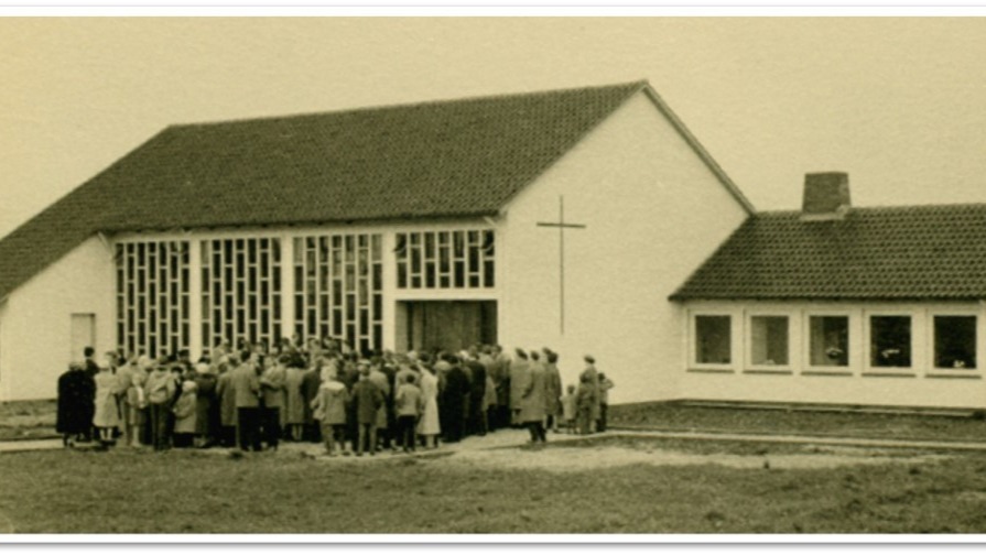 Viele Menschen versammeln sich vor der Mennonitenkirche mit einem großen Kreuz und vertikalen Fenstern auf einer Wiese