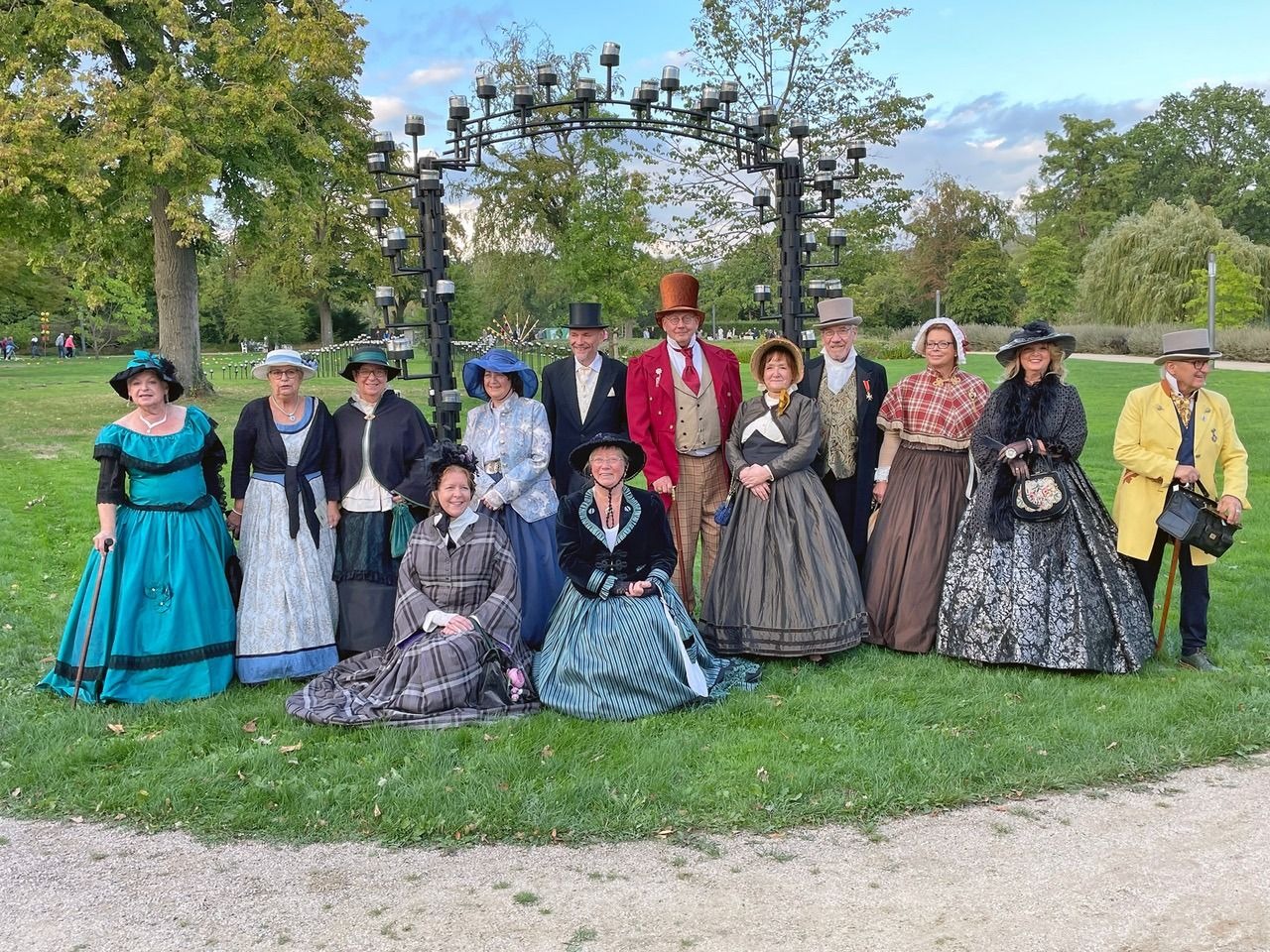 Dreizehn Personen in historischen Kleidern posieren im Kurpark vor einem Metallbogen mit Lichtern