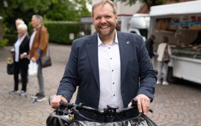 Lemmen lacht breit, hält die Lenker eines Lastenrads, hinter ihm Menschen und ein Imbisswagen