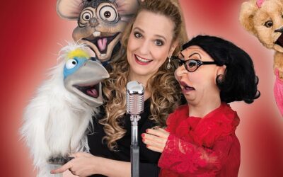 Murzarella lächelt mit einem Mikrofon und vier Puppen: einem Vogel, einer Ratte, einer Dame und einem Löwen