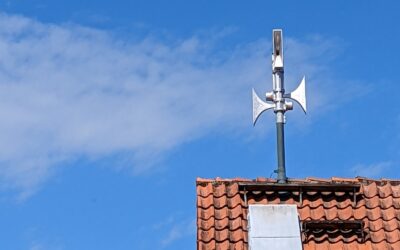 Eine metallene Sirene mit mehreren Lautsprechern auf einem roten Ziegeldach unter blauem Himmel