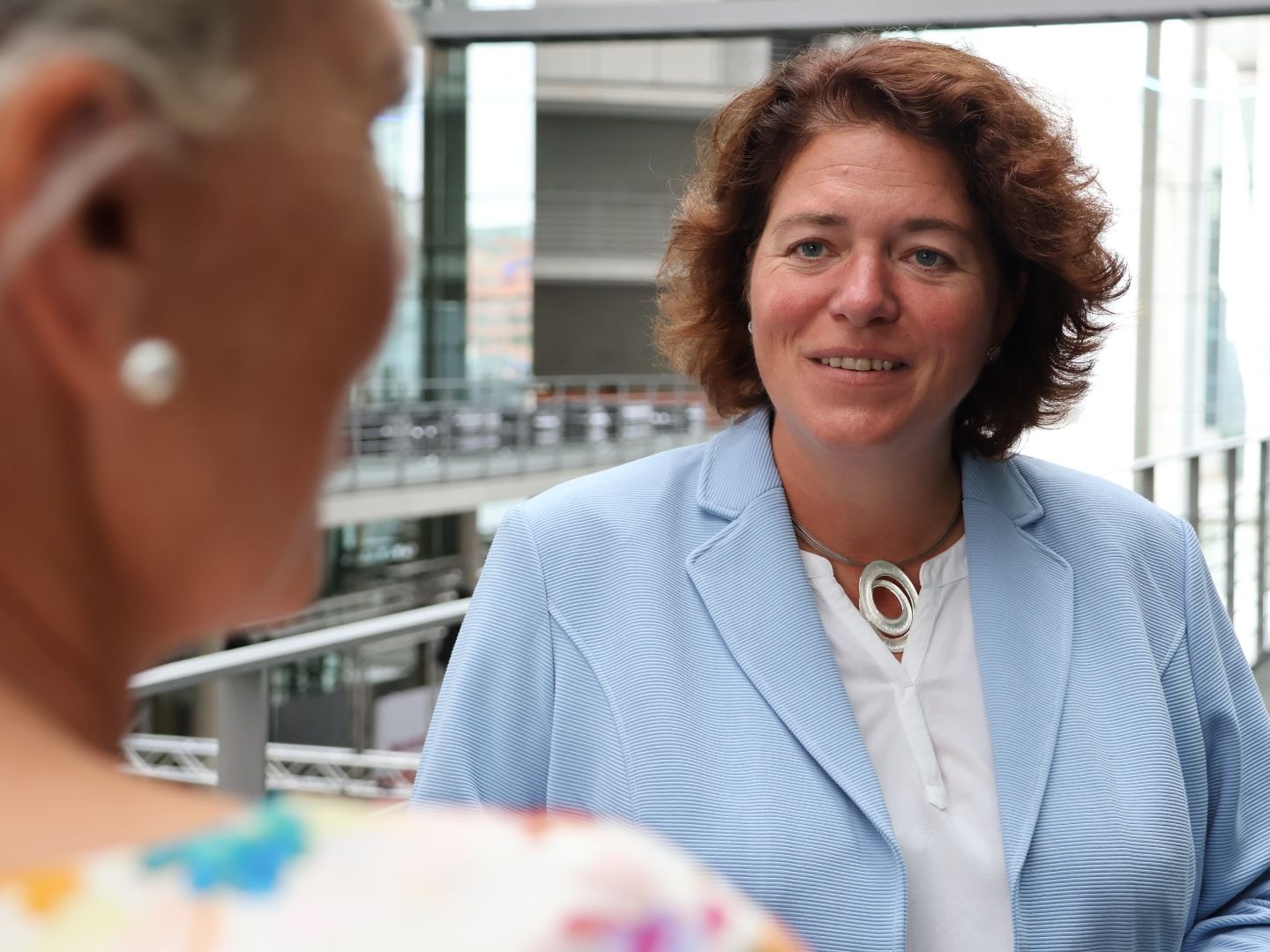 MdB Kerstin Vieregge lächelt eine Person in einem modernen Bürogebäude an