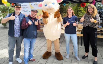 Vier Personen und ein Ziegen-Maskottchen geben Daumen hoch vor einem Weltkindertag-Banner und Zelt