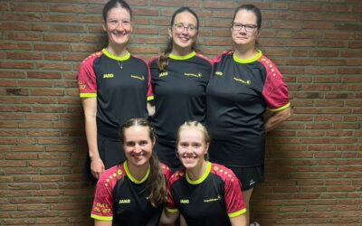 Fünf Frauen in schwarzen Sportshirts und Röcken lächeln, drei stehend und zwei kniend, vor einer Ziegelwand