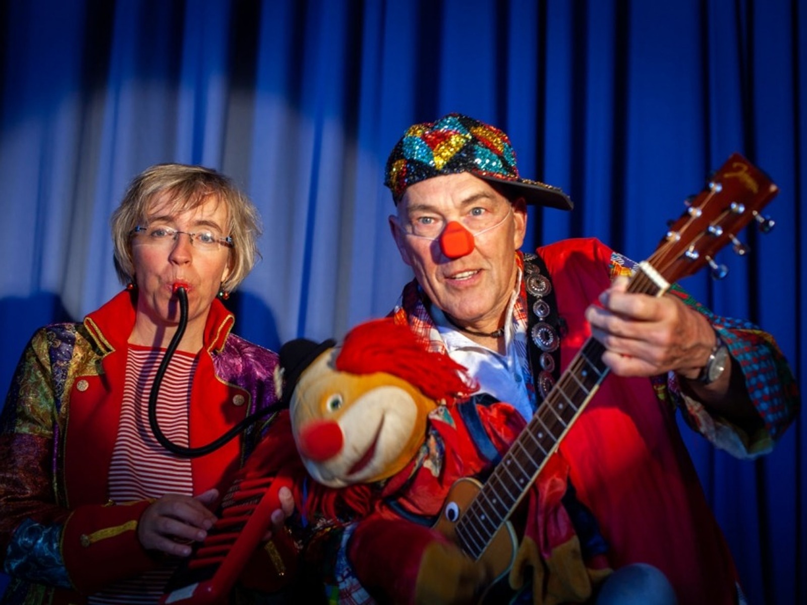Zwei Künstler auf der Bühne: Eine Frau spielt Melodica, ein Mann mit Clownsnase und bunter Kappe spielt Gitarre mit