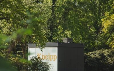 Modernes Kneipp-Gebäude mit Schriftzug umgeben von Bäumen und Büschen im Landschaftsgarten